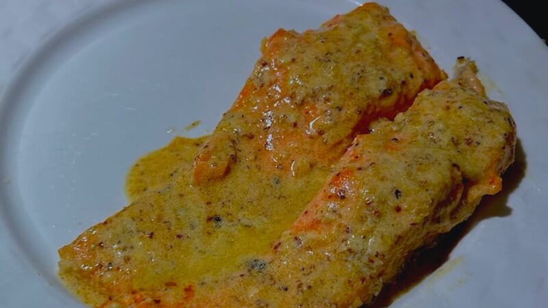 A serving of baked salmon with lemon butter cream sauce on a plate.