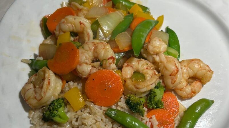 Cover image for shrimp stir-fry recipe. Features a close up of a plate of shrimp, carrots, snap peas, and brown rice.